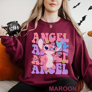 Peut inclure: Sweat-shirt bordeaux avec un personnage de dessin anim&eacute; Angel et le texte "ANGEL" dans une police r&eacute;tro. Le motif comprend des fleurs et un ballon bleu en forme de Mickey Mouse. Le mot "MAROON" est en bas.