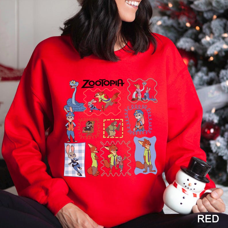 Puede incluir: Una sudadera roja con un dise&ntilde;o gr&aacute;fico colorido con personajes y la palabra "ZOOTOPIA". El dise&ntilde;o incluye varias im&aacute;genes enmarcadas de personajes de la pel&iacute;cula animada. La sudadera es de color rojo liso.