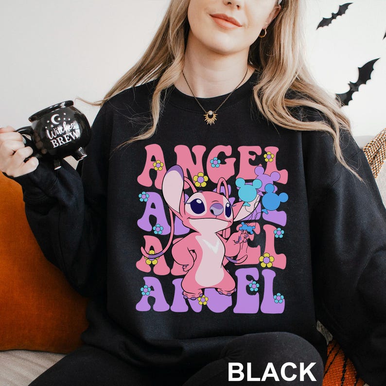 Peut inclure: Sweat-shirt noir avec le mot "ANGEL" en rose et violet dans une police r&eacute;tro, et un personnage de dessin anim&eacute; au centre. Le personnage est rose et tient des objets bleus. Le mot "BLACK" est en bas.