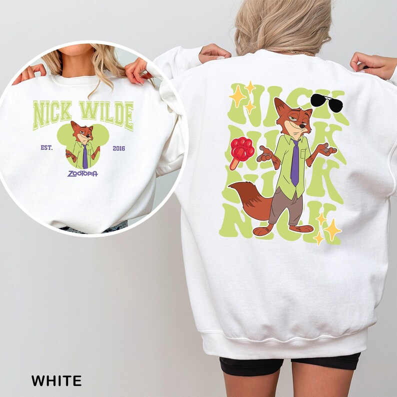 Puede incluir: Sudadera blanca con una imagen de dibujos animados de Nick Wilde de Zootopia. La parte delantera tiene un dise&ntilde;o circular con el texto "Nick Wilde" y "Zootopia". La parte trasera muestra una imagen m&aacute;s grande de Nick Wilde con gafas de sol y un helado, rodeado de texto verde.