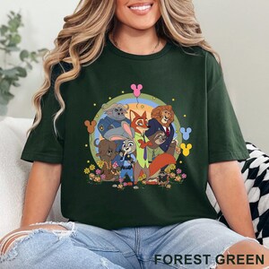 Puede incluir: Camiseta verde bosque con un dise&ntilde;o de dibujos animados de personajes animales, un arco&iacute;ris, flores y globos con forma de Mickey Mouse. El texto "FOREST GREEN" est&aacute; impreso en la parte inferior.