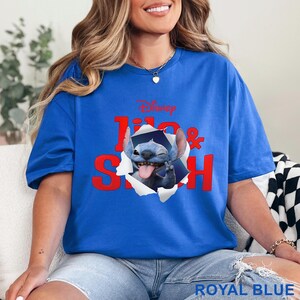 May include: Royal blue t-shirt featuring the Disney characters Lilo & Stitch. The design shows Stitch popping out of a torn paper effect, sticking out his tongue and flashing a peace sign. The text "Disney Lilo & Stitch" is in red.