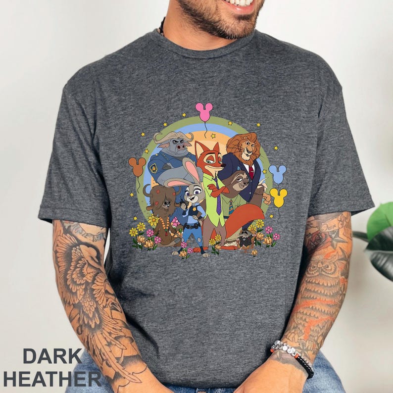 Puede incluir: Camiseta gris jaspeado oscuro con una colorida ilustraci&oacute;n de dibujos animados de los personajes de Zootopia, incluyendo a Judy Hopps y Nick Wilde. El dise&ntilde;o presenta flores, iconos de Mickey Mouse y el texto "DARK HEATHER" en la parte inferior.