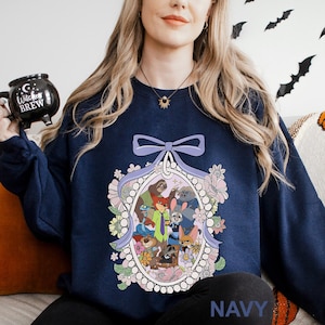 May include: Navy blue sweatshirt with a cartoon character design inside a floral frame, topped with a lavender bow. The word "NAVY" is printed at the bottom. A comfortable, casual style.