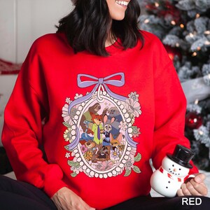 May include: A red sweatshirt with a cartoon illustration of animal characters in an oval frame, decorated with flowers and a purple bow. The word "RED" is printed in white at the bottom right of the image.