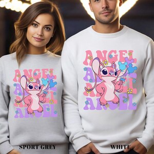 Peut inclure: Sweat-shirts gris sport et blancs avec un personnage de dessin anim&eacute; rose tenant des ballons bleus et violets. Le mot "ANGEL" est imprim&eacute; en rose, violet et lavande, avec de petits motifs floraux. Port&eacute;s par une femme et un homme.
