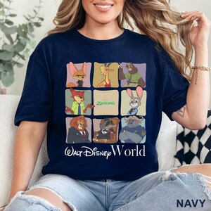 Puede incluir: Camiseta azul marino con un dise&ntilde;o de cuadr&iacute;cula que muestra personajes de la pel&iacute;cula Zootopia, con la frase "Walt Disney World" debajo. El dise&ntilde;o incluye a Nick Wilde, Judy Hopps y otros personajes. La palabra "NAVY" est&aacute; impresa en la parte inferior derecha.