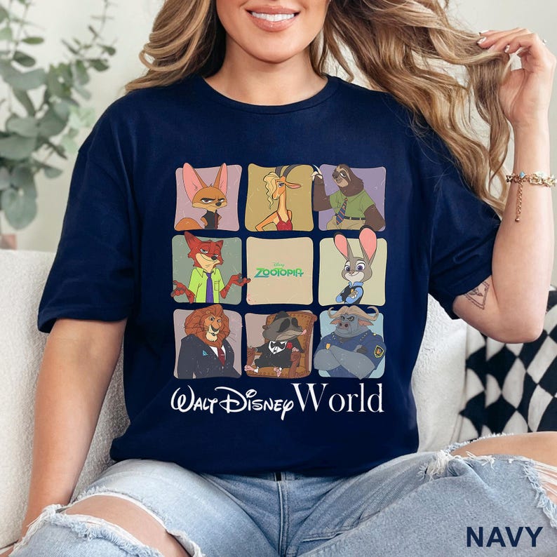 Puede incluir: Camiseta azul marino con un dise&ntilde;o de cuadr&iacute;cula que muestra personajes de la pel&iacute;cula Zootopia, con la frase "Walt Disney World" debajo. El dise&ntilde;o incluye a Nick Wilde, Judy Hopps y otros personajes. La palabra "NAVY" est&aacute; impresa en la parte inferior derecha.