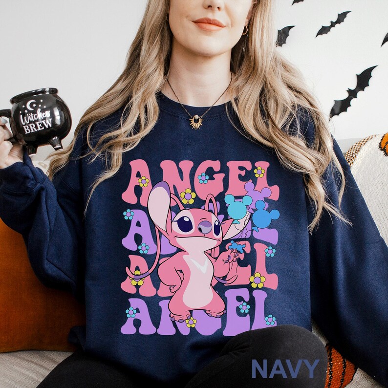 Peut inclure: Sweat-shirt bleu marine avec un personnage de dessin anim&eacute; rose et le mot "ANGEL" dans une police r&eacute;tro. Le motif comprend des fleurs et des &eacute;l&eacute;ments en forme de Mickey Mouse. Le mot "NAVY" est imprim&eacute; en bas.