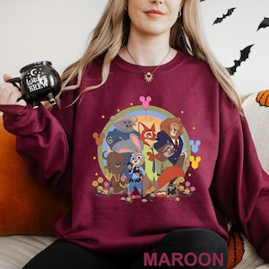 May include: Maroon sweatshirt with a colourful graphic of animated movie characters. The design includes a circle with a rainbow, flowers, and cartoon animals. The word "MAROON" is printed at the bottom.