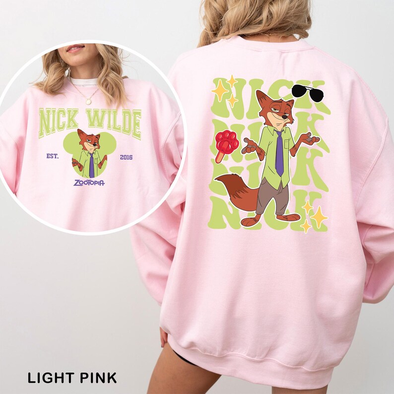 Puede incluir: Sudadera rosa claro con una ilustraci&oacute;n de dibujos animados de Nick Wilde de Zootopia. La parte delantera muestra "Nick Wilde" y "Zootopia". La parte trasera presenta una imagen m&aacute;s grande de Nick Wilde con gafas de sol y un helado, y el texto "Nick Wilde".
