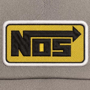 May include: Close-up of a gray baseball cap with a rectangular patch. The patch features the black letters "NOS" on a yellow background, outlined in white. An arrow points right. The cap is made of a textured fabric.