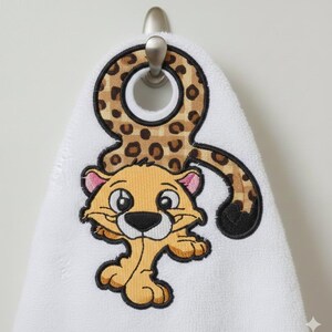 May include: White hand towel with an embroidered cartoon cheetah design. The cheetah has a tan body, pink ears, and a black nose. The towel's top portion features a cheetah print pattern.