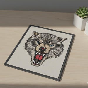 May include: Embroidered rectangular patch featuring a detailed wolf head with blue eyes and an open mouth, showcasing sharp teeth and a red tongue. The design is set against a light beige background with a dark gray border. The patch is likely for apparel or accessories.
