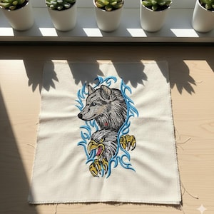 May include: Embroidered patch with a wolf and eagle design. The wolf is grey and the eagle is white and yellow, with blue accents. The patch is on a beige fabric.