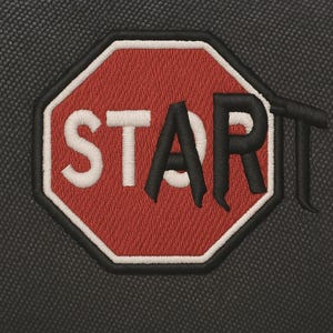 Könnte beinhalten: Gestickter Aufnäher in Form eines Stoppschildes mit dem Wort "START" in weißen und schwarzen Buchstaben. Der Aufnäher hat einen roten Hintergrund mit weißem Rand, vor einem strukturierten schwarzen Stoff.