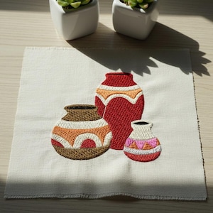 May include: Embroidered artwork featuring three decorative vases in shades of red, brown, orange, and pink. The vases are set against a cream-colored fabric background. The design showcases detailed stitching and a rustic aesthetic.