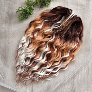 May include: A bundle of wavy hair extensions in a mix of colors, including dark brown, light brown, white, and a golden blonde. The hair is styled in loose, flowing waves, with a natural-looking gradient effect. The extensions are likely for adding length or volume to existing hair.