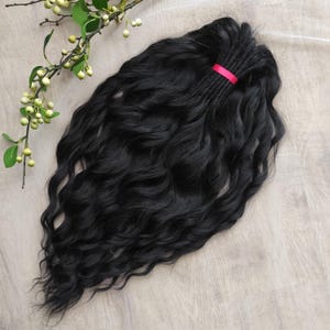 May include: A long, black, wavy hair extension with a pink elastic band tied around the top.