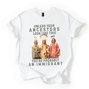 May include: White t-shirt with the text "UNLESS YOUR ANCESTORS LOOK LIKE THIS YOU'RE PROBABLY AN IMMIGRANT" above a graphic of three Native American figures in traditional clothing.