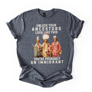 May include: A heather gray t-shirt with the text "UNLESS YOUR ANCESTORS LOOK LIKE THIS YOU'RE PROBABLY AN IMMIGRANT." The shirt features a graphic of three Native American figures in traditional clothing.