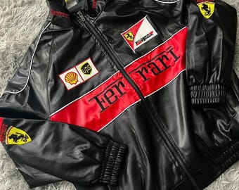 以下が含まれることがあります： 赤と白のアクセントが施された黒いフェラーリレーシングジャケット。フェラーリ、UPS、F-1のパッチが特徴です。ジャケットはジッパー開閉、白いパイピング、リブ編みの袖口を備えています。モータースポーツをテーマにした衣服。