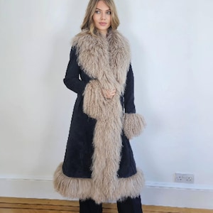 May include: A long, dark navy coat with a beige fur collar, cuffs, and hem. The coat is worn over dark trousers and shoes. The fur trim adds a luxurious texture to the outerwear. The coat is a stylish fashion statement.