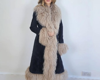 Può includere: Un cappotto lungo blu navy scuro con collo, polsini e orlo in pelliccia beige. Il cappotto è indossato sopra pantaloni e scarpe scure. L'applicazione in pelliccia aggiunge una texture lussuosa all'outerwear.