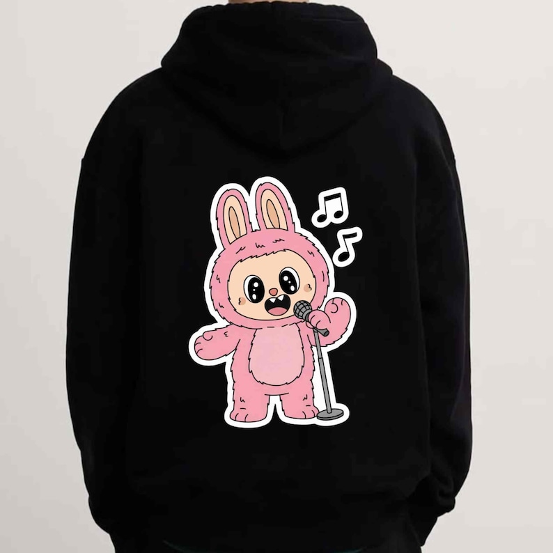 May include: Black hoodie featuring a cartoon bunny character in a pink costume holding a microphone. The bunny has large eyes and is singing, with musical notes above its head. The hoodie has a drawstring hood.