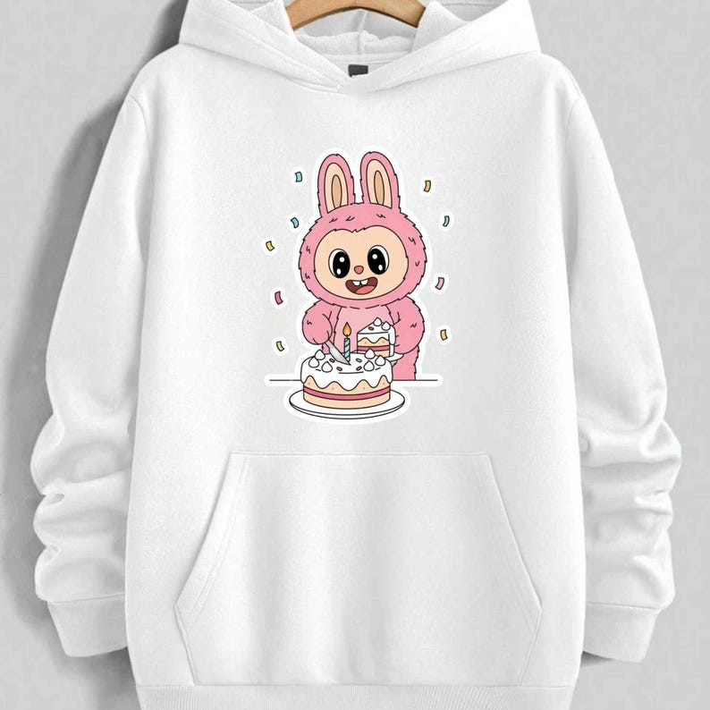 May include: White hooded sweatshirt featuring a pink cartoon bunny character holding a birthday cake with a lit candle. The bunny is surrounded by confetti. The design is centered on the front of the sweatshirt, with a kangaroo pocket below.