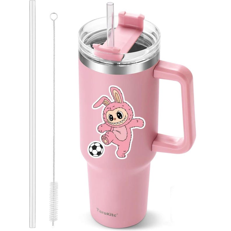 May include: A pink insulated tumbler with a handle, a clear lid, and a pink straw. A sticker of a cartoon bunny playing soccer is on the side. Includes a clear straw and a cleaning brush. The brand name "TaroKite" is printed on the bottom.