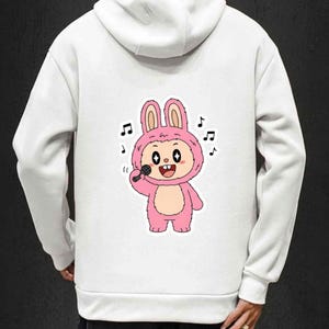 May include: White hoodie featuring a cartoon bunny character in a pink costume holding a microphone. The bunny is surrounded by musical notes. The hoodie has a drawstring hood and long sleeves.