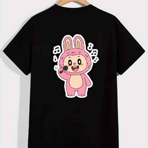 May include: Black t-shirt featuring a cartoon bunny character in a pink costume holding a microphone. The bunny is singing, with musical notes around it. The design is a fun and playful graphic.