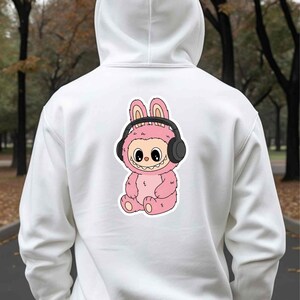 May include: White hoodie with a pink cartoon character wearing headphones. The character has bunny ears and a smiling face. The design is centered on the back of the hoodie.