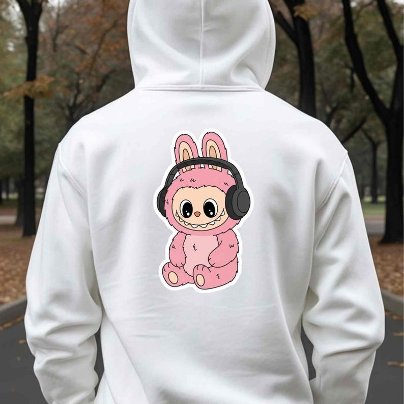 May include: White hoodie with a pink cartoon character wearing headphones. The character has bunny ears and a smiling face. The design is centered on the back of the hoodie.