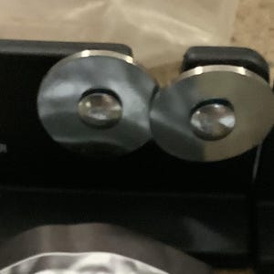 May include: Black knife sharpener with two silver sharpening wheels. The text "RADA Mfg. Co. QUICK EDGE KNIFE SHARPENER" is printed in white on the black base. The sharpener is designed for quick and easy knife sharpening.