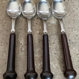 May include: A set of four spoons featuring polished silver-tone metal bowls and long, smooth, dark brown cylindrical handles that flare slightly at the base. Each spoon has a consistent design with a metal bolster connecting the bowl to the handle.