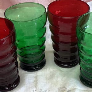 May include: Four vintage drinking glasses in red and green. The glasses have a unique, ribbed design and a dark base. Two are red, and two are green, offering a colorful set for beverages.
