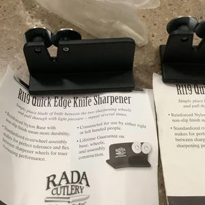 May include: Black R119 Quick Edge Knife Sharpener with two sharpening wheels. The product features a reinforced nylon base and a standardized rivet/wheel assembly. The packaging includes the RADA CUTLERY logo and product information.