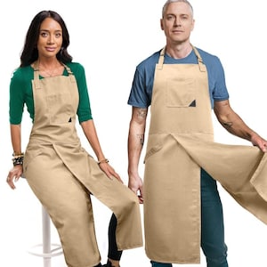 Może przedstawiać: Dwie osoby w beżowych fartuchach z kieszenią i czarnym trójkątnym detalem. Fartuchy mają owijany krój. Jedna osoba ma na sobie zieloną koszulę, a druga niebieską. Fartuchy są wykonane z wytrzymałej tkaniny.