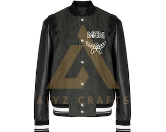 Puede incluir: Una chaqueta de béisbol gris y negra con mangas de cuero. La chaqueta tiene un cuello, puños y cintura de punto de canalé blanco y negro. La chaqueta tiene un logotipo MCM bordado en blanco en el pecho izquierdo.