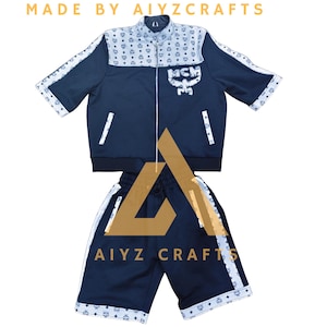 Op de afbeelding: Een set bestaande uit een marineblauw jack met korte mouwen en rits en een bijpassende korte broek, voorzien van witte panelen met een herhalend MCM-logopatroon. Het jack heeft een wit MCM-logo op de borst en witte biezen. De tekst luidt MADE BY AIYZCRAFTS.
