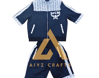 May include: A navy blue short-sleeve zip-up jacket and matching shorts set featuring white panels with a repeating MCM logo pattern. The jacket includes a white MCM logo graphic on the chest and white trim along the sleeves and pockets. Text reads MADE BY AIYZCRAFTS.