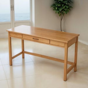 May include: A light wood desk with two drawers and a simple design. The desk has a natural wood finish and is made of solid wood.