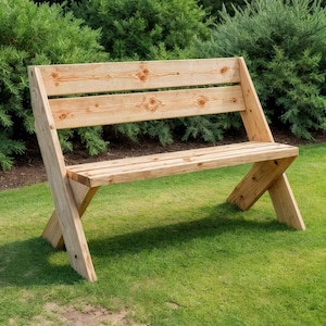 Könnte beinhalten: Eine Holzbank mit natürlichem Finish, auf einem Rasen platziert. Die Bank hat eine Sitzfläche und Rückenlehne aus Latten, mit einem X-förmigen Beindesign. Die Bank ist aus hellfarbigem Holz gefertigt und von grünem Laub umgeben.