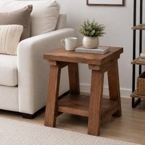 Könnte beinhalten: Ein quadratischer Beistelltisch aus Holz mit dunkelbraunem Finish, vier stabilen Beinen und einer unteren Ablage. Auf der Tischplatte stehen eine weiße Keramiktasse, ein Buch mit dem Titel Made for Living und eine kleine grüne Topfpflanze.