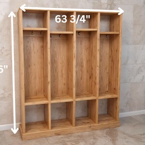 May include: A wooden storage unit with multiple compartments, shelves, and hooks. The unit is 76 inches tall and 63 3/4 inches wide. It is constructed from light-colored wood and has a natural finish, suitable for organizing items.
