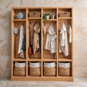 May include: A wooden entryway organizer with multiple compartments. It features hooks for hanging coats and hats, baskets for storage, and shelves for decorative items. The organizer is made of light-colored wood and is set against a neutral-toned tiled wall.
