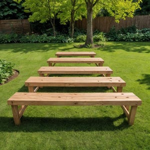 May include: A series of five wooden benches arranged in a descending row on a green lawn. The benches are made of light-colored wood and have a simple, rectangular design. The background features trees, grass, and a wooden fence.