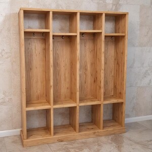May include: A wooden storage unit with multiple compartments. The unit is made of light-colored wood and features open shelves and hooks for hanging items. The design is simple and functional, suitable for organizing various items.